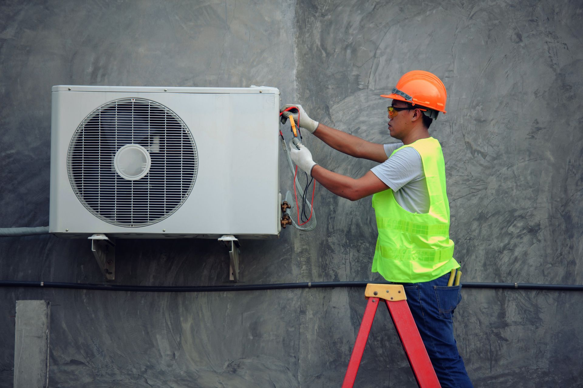 A man wearing a green vest is engaged in air conditioner repair, demonstrating safety and expertise.