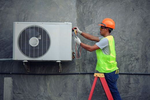 A man wearing a green vest is engaged in air conditioner repair, demonstrating safety and expertise.