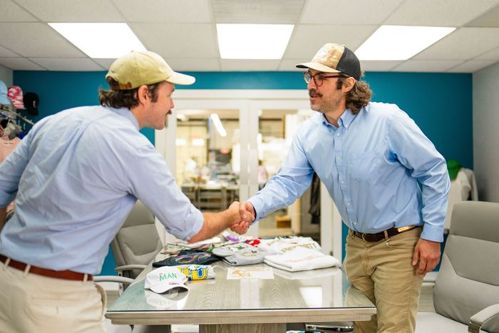 Two men are shaking hands over a table in an office.