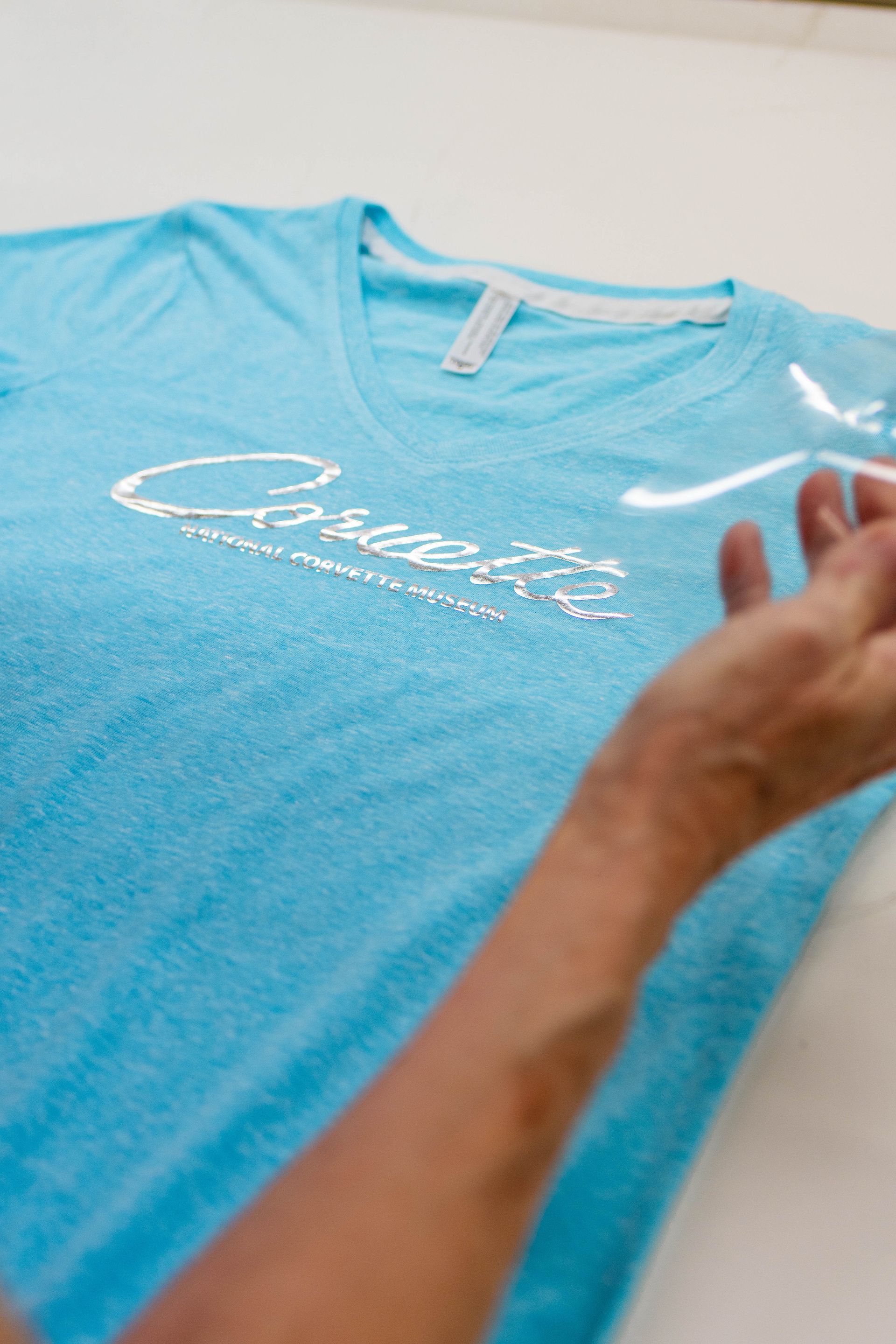 A person is applying vinyl to a blue t-shirt.