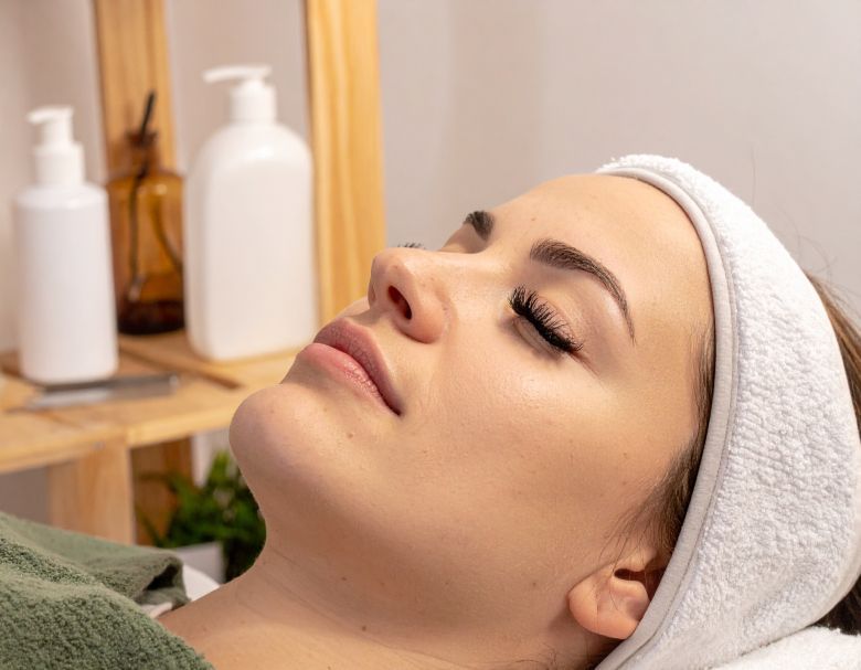 Woman with eyes closed, wearing a headband, relaxing on a treatment table. Spa setting with skincare products.