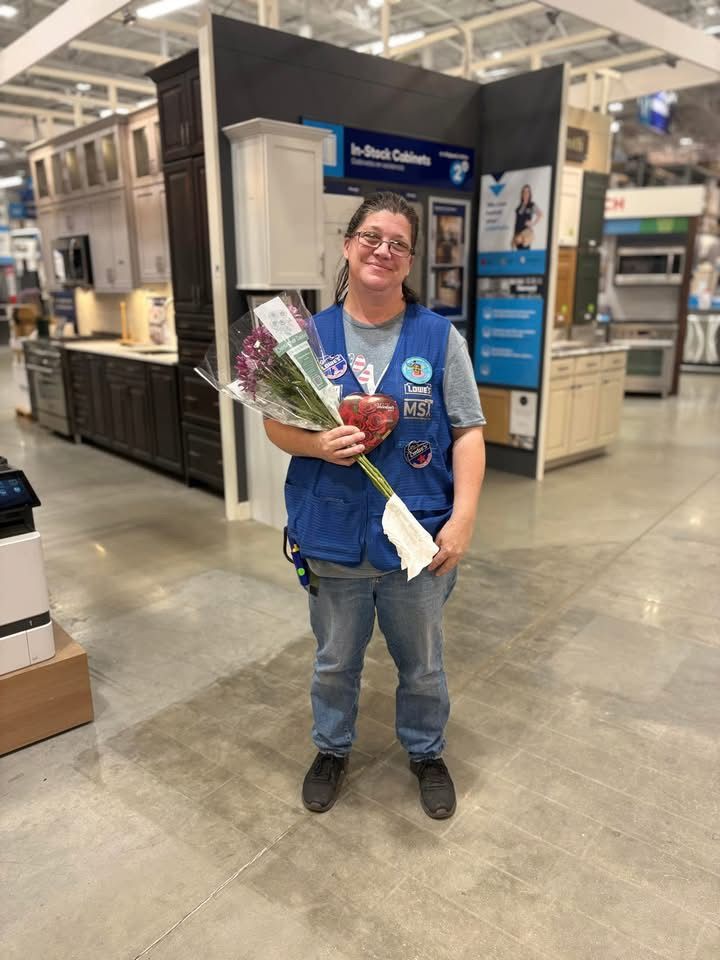 A woman in a blue vest is holding a bouquet of flowers in a store.