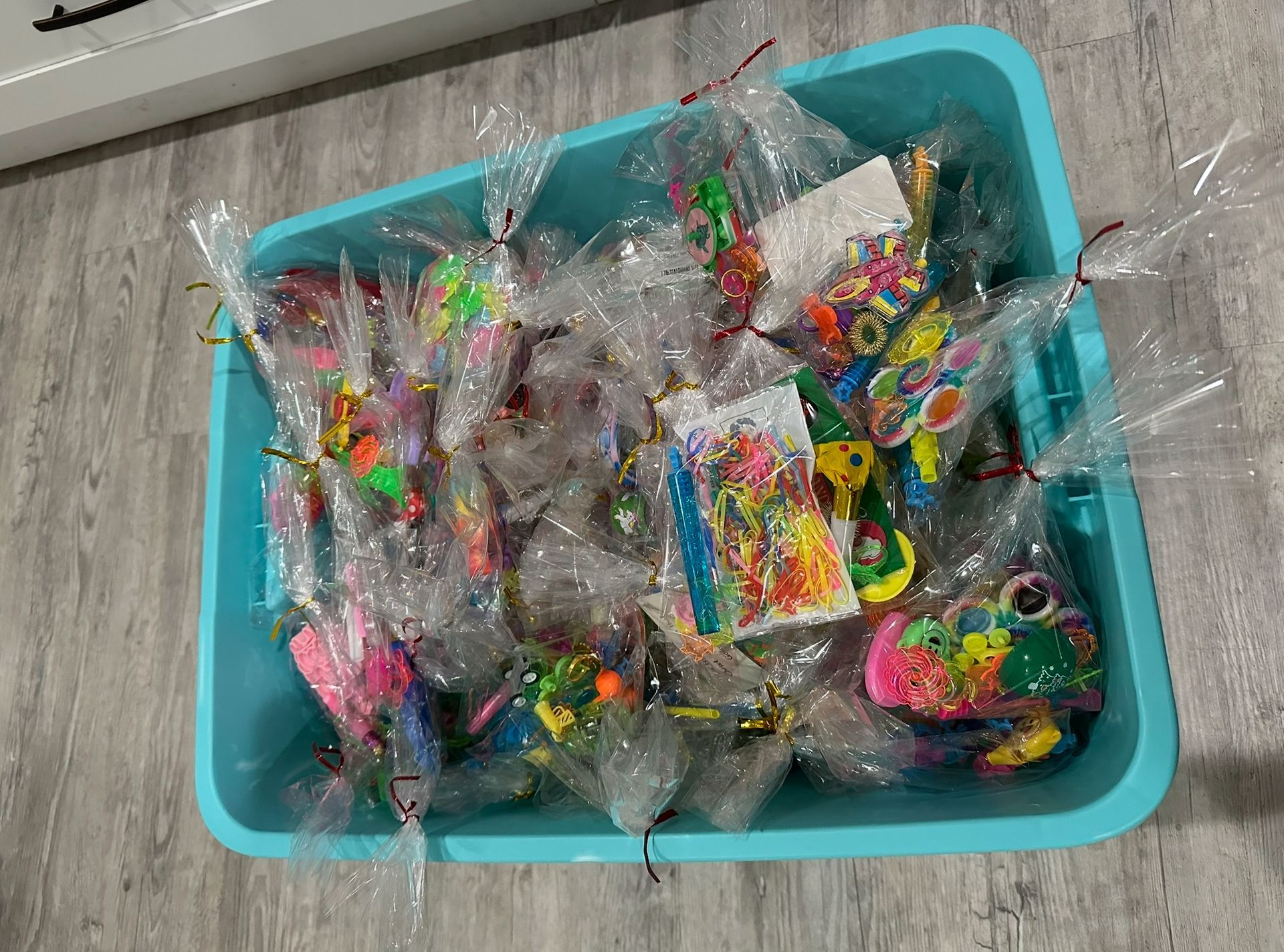 A blue tray filled with plastic bags of toys on a wooden floor.