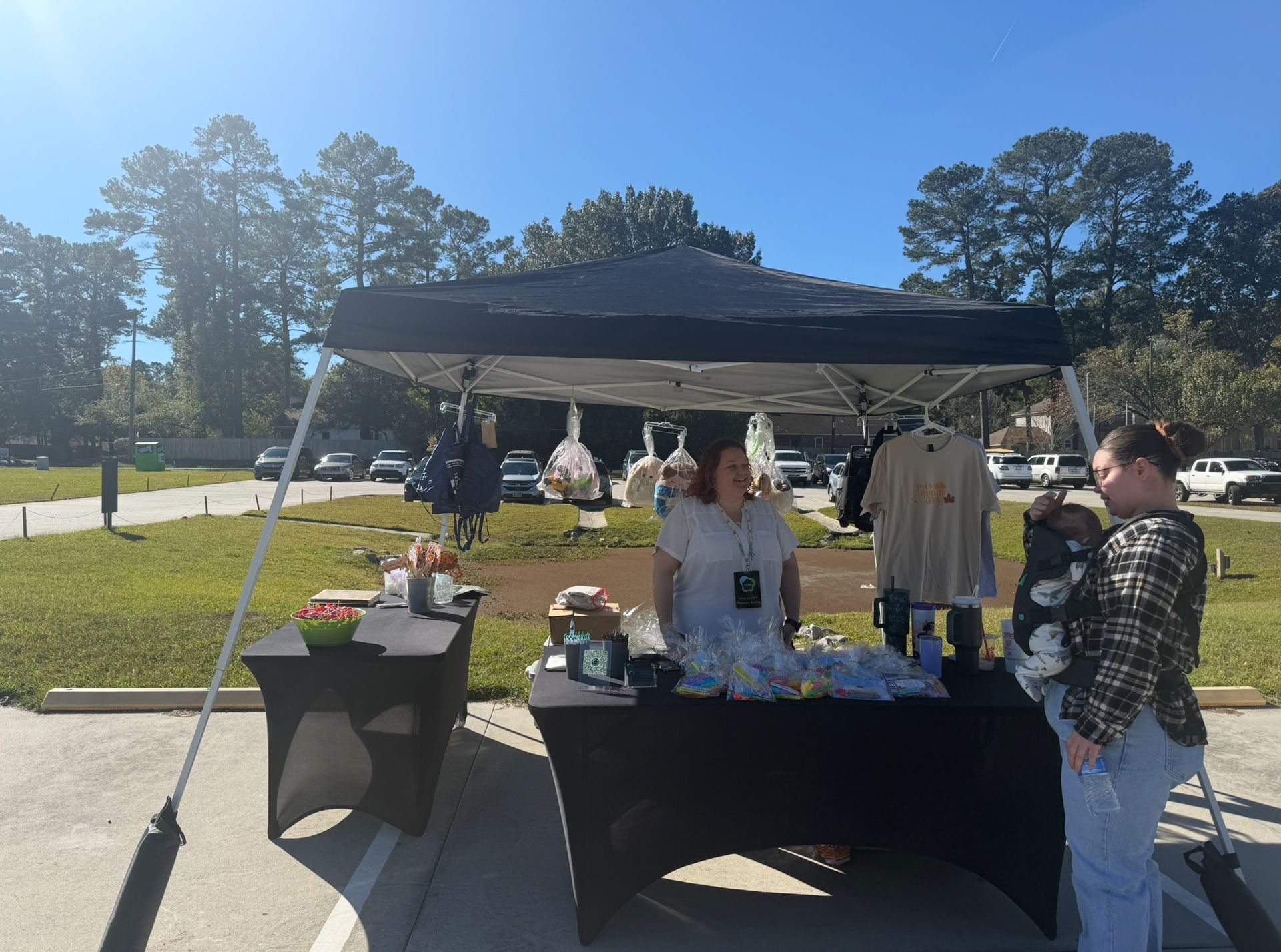 A woman is standing at a table under a tent in a parking lot.