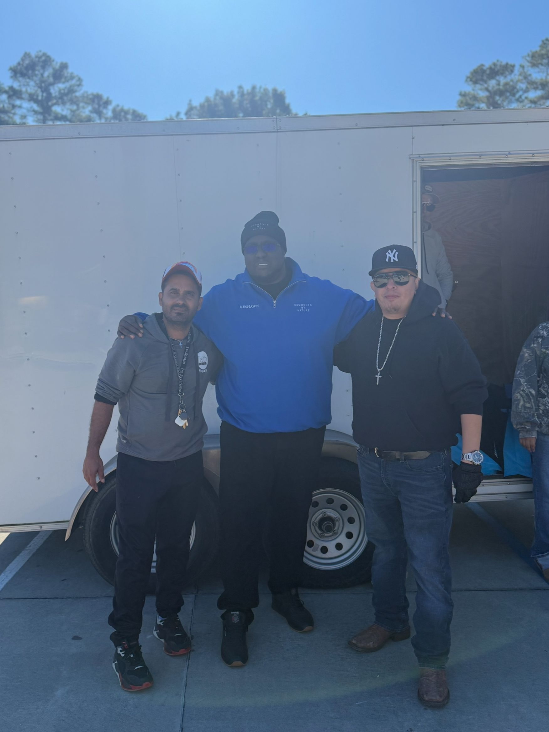 Three men are posing for a picture in front of a white trailer
