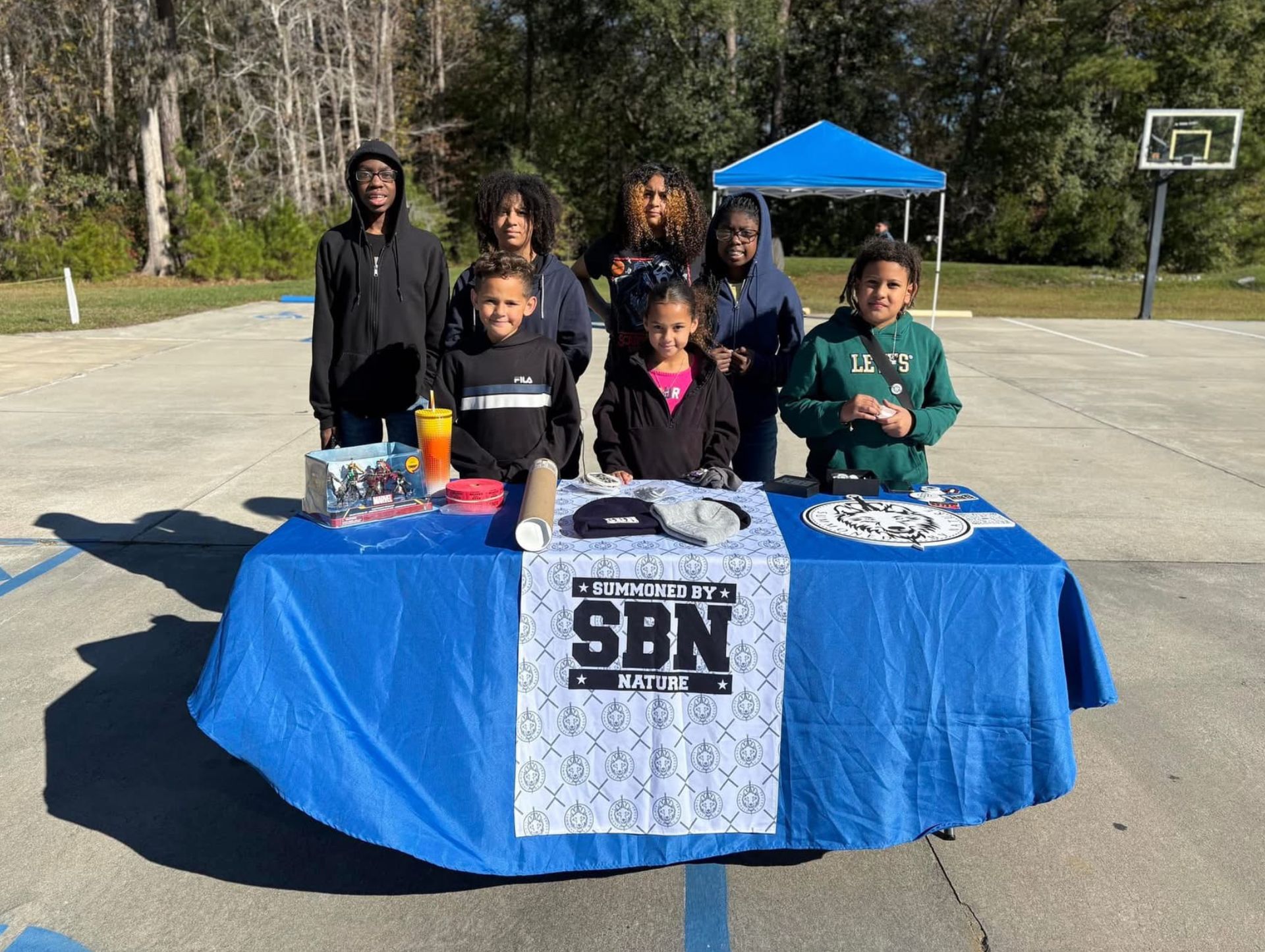 A group of children are standing around a table with a blue table cloth.