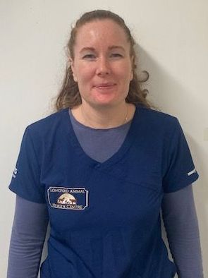 A woman in a blue scrub top is standing in front of a white wall.