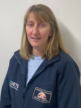 A woman wearing a blue jacket is standing in front of a white wall.