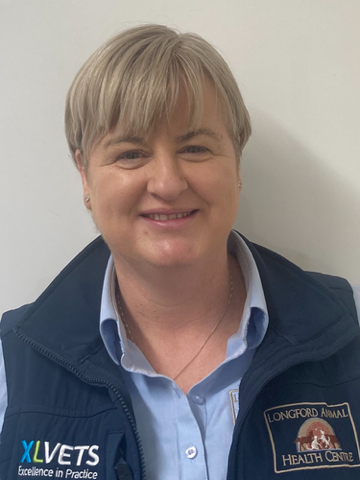 A woman wearing a blue vest and a blue shirt is smiling for the camera.