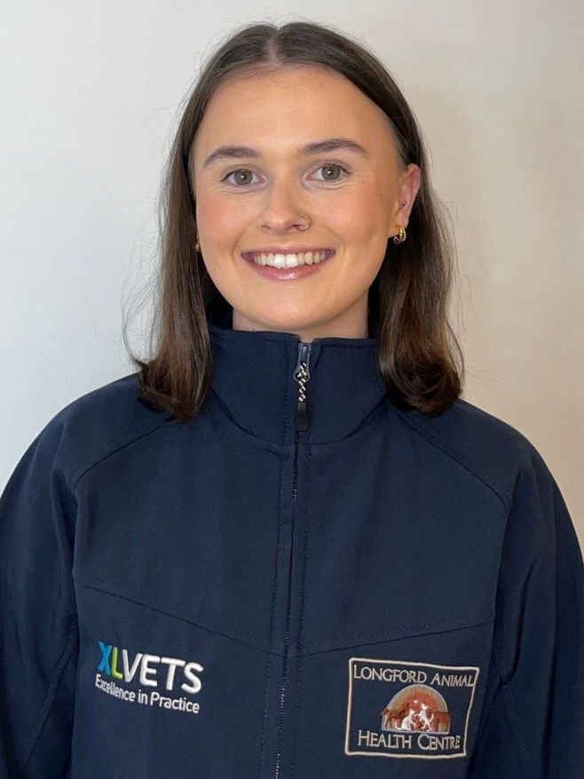 A woman wearing a blue jacket with xlvets written on it is smiling.