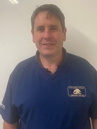 A man in a blue shirt is standing in front of a white wall.