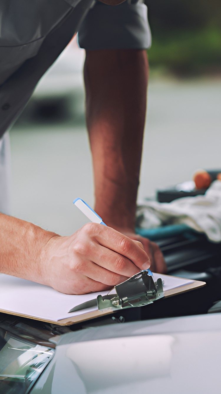 A Man Is Writing On A Clipboard In Front Of A Car — Warrmech Mechanical In Tweed Heads South, NSW