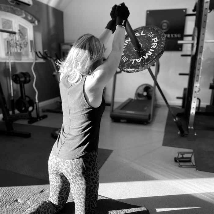 Woman in gym kneeling, lifting barbell overhead, with weight plates.