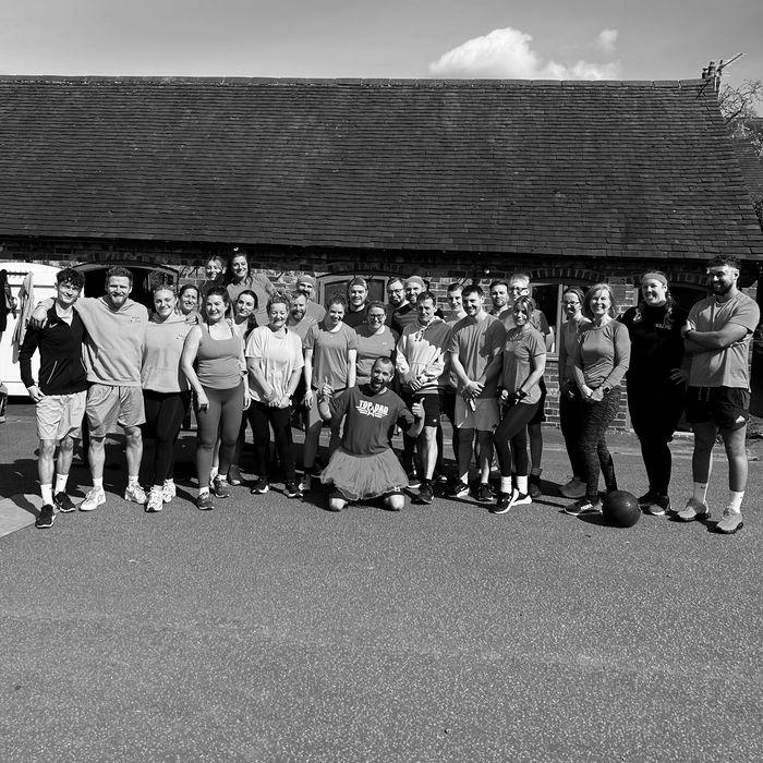 Group of people posing outdoors in front of a thatched-roof building.