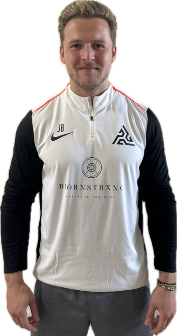 Man with blond hair in a white and black shirt with a logo, stands smiling.