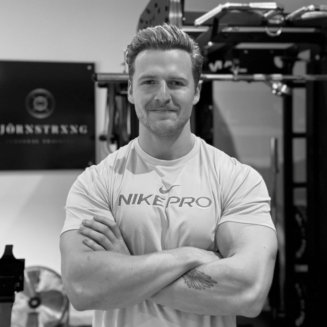 Man with crossed arms in a gym, wearing a Nike Pro shirt. Black and white photo.