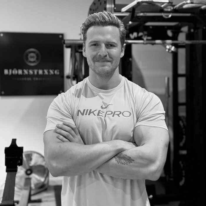 Four women in a gym, holding dumbbells, wearing white shirts with logos, smiling.