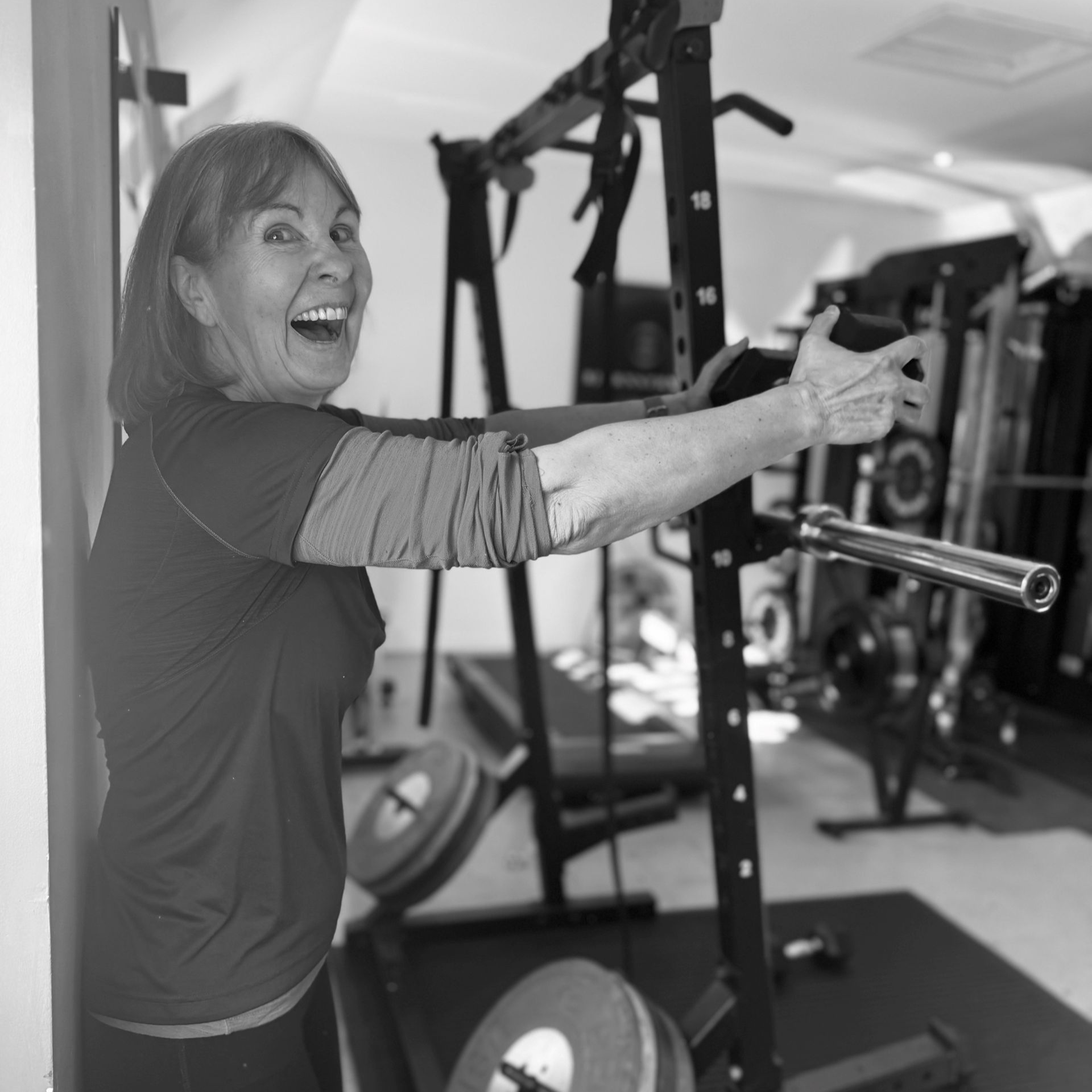 Woman excitedly points in a home gym. She stands near weight equipment, smiling.