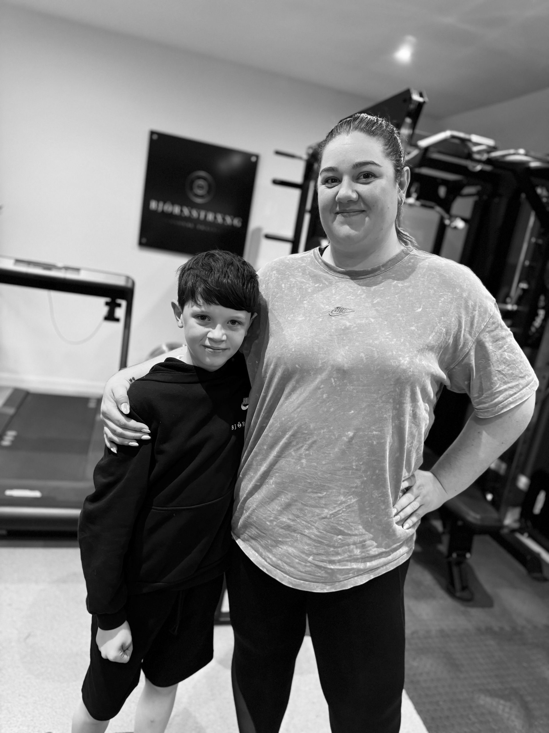 Woman with arm around boy in a gym setting, both smiling. Black and white photo.