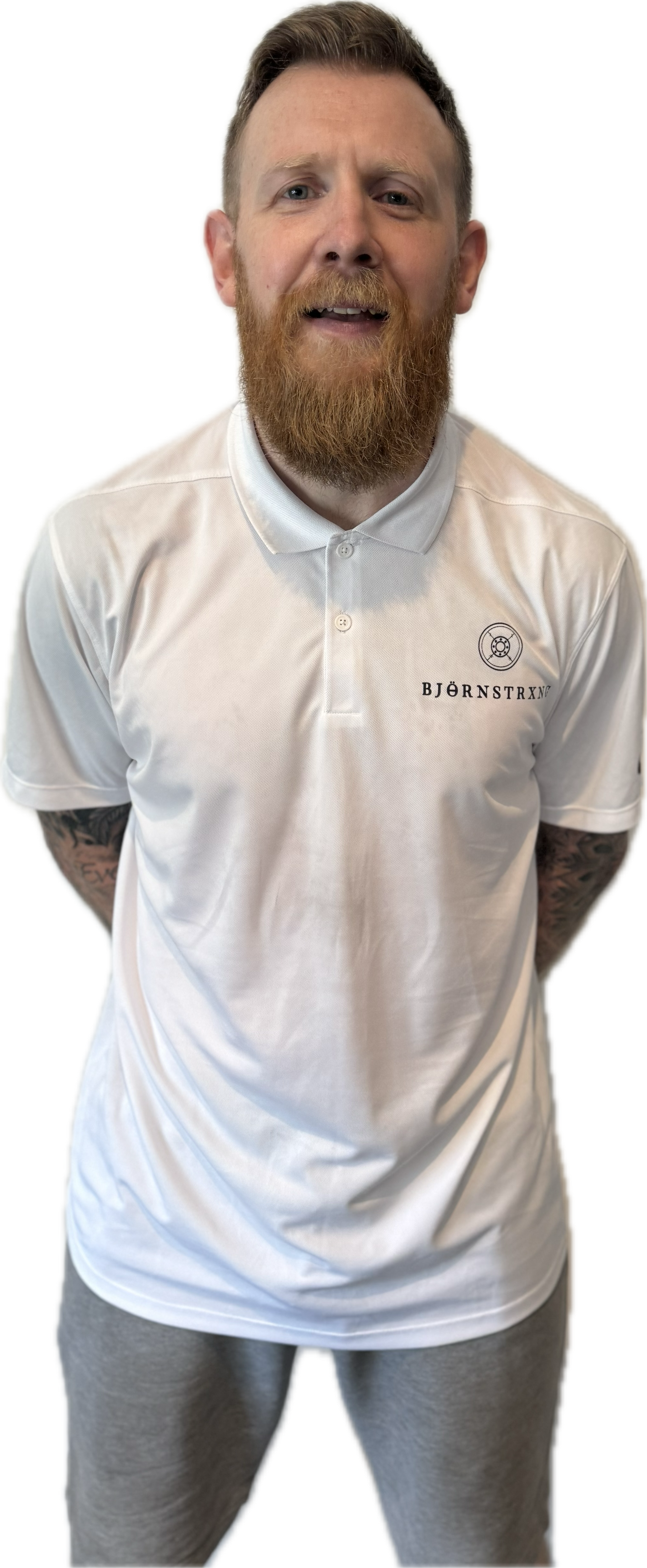 Man with a beard wearing a white polo shirt and gray pants, standing with hands behind back.