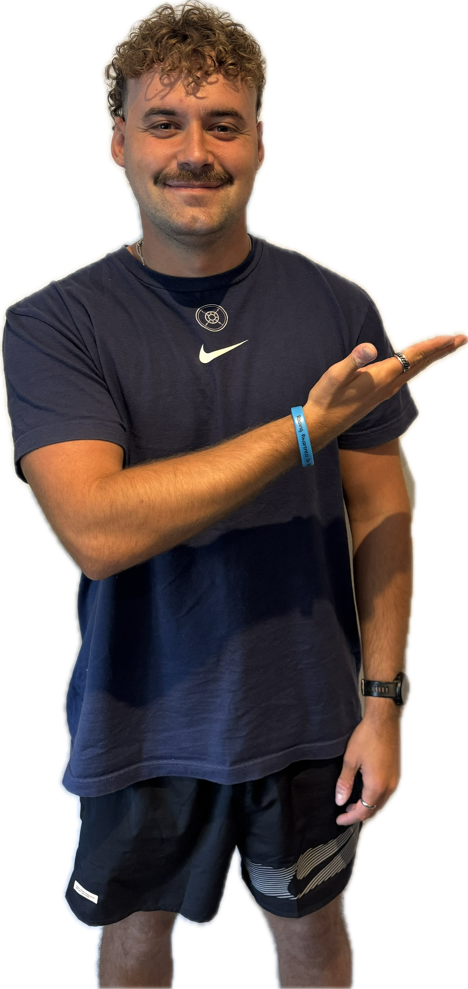 Man with curly hair and mustache in navy shirt and black shorts, pointing to the right.
