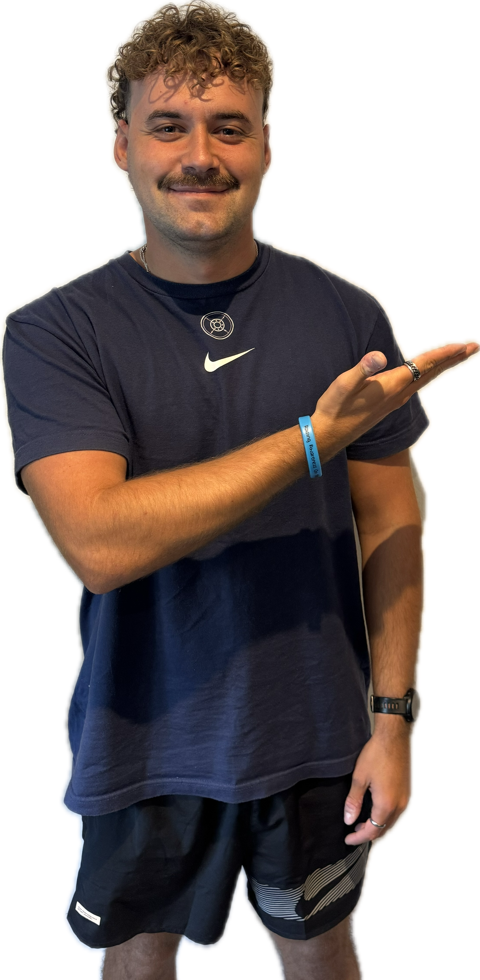 Man with curly hair and mustache in navy shirt and black shorts, pointing to the right.