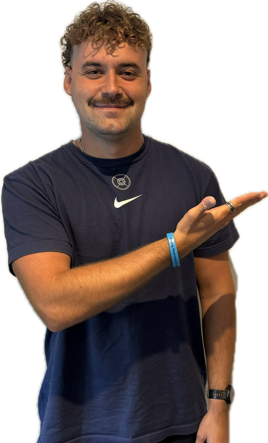 Man in navy shirt pointing to the right, smiling. Curly brown hair, mustache, and a blue wristband.