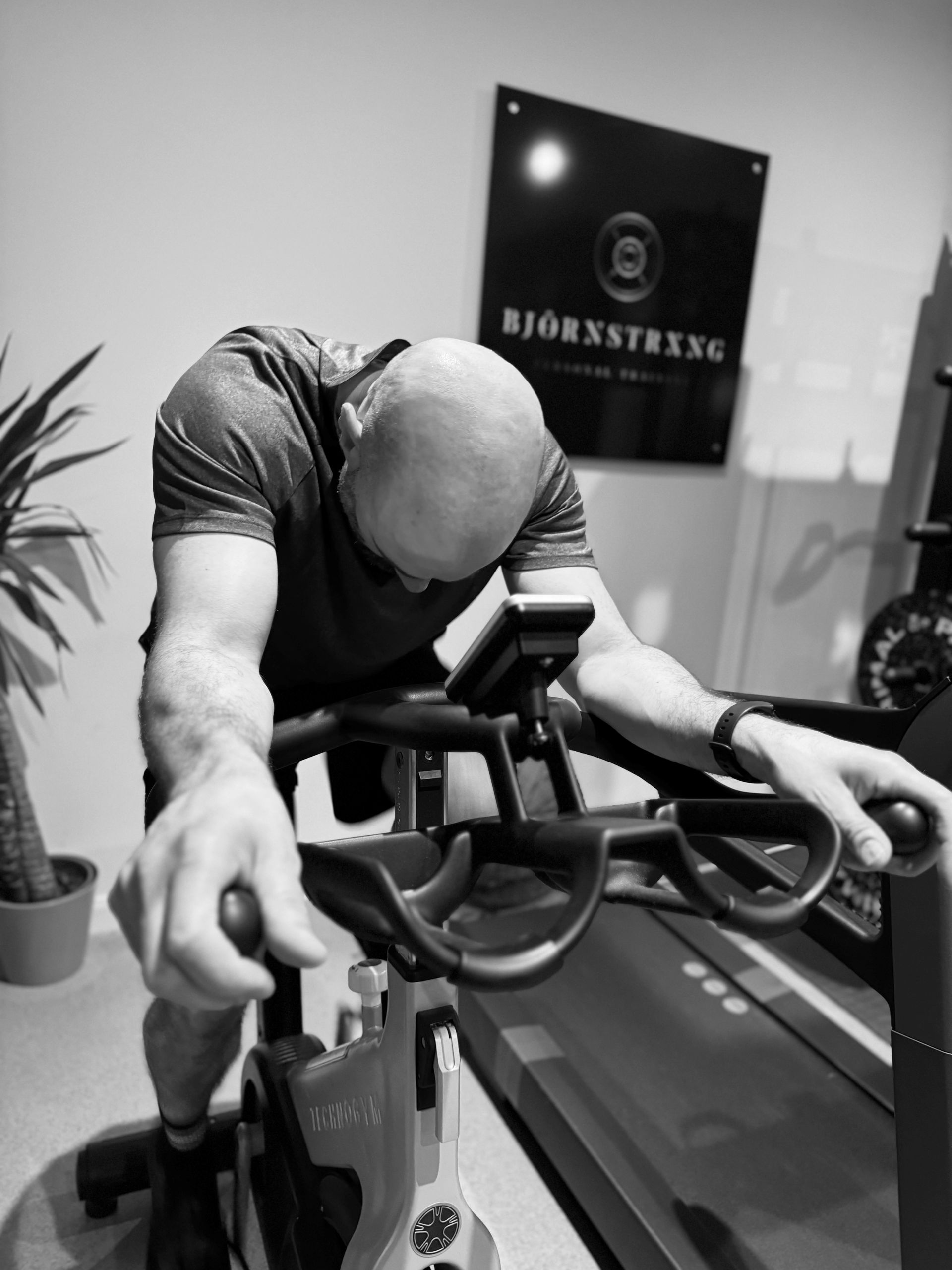 Man on a stationary bike, head down, in gym, with a plaque saying