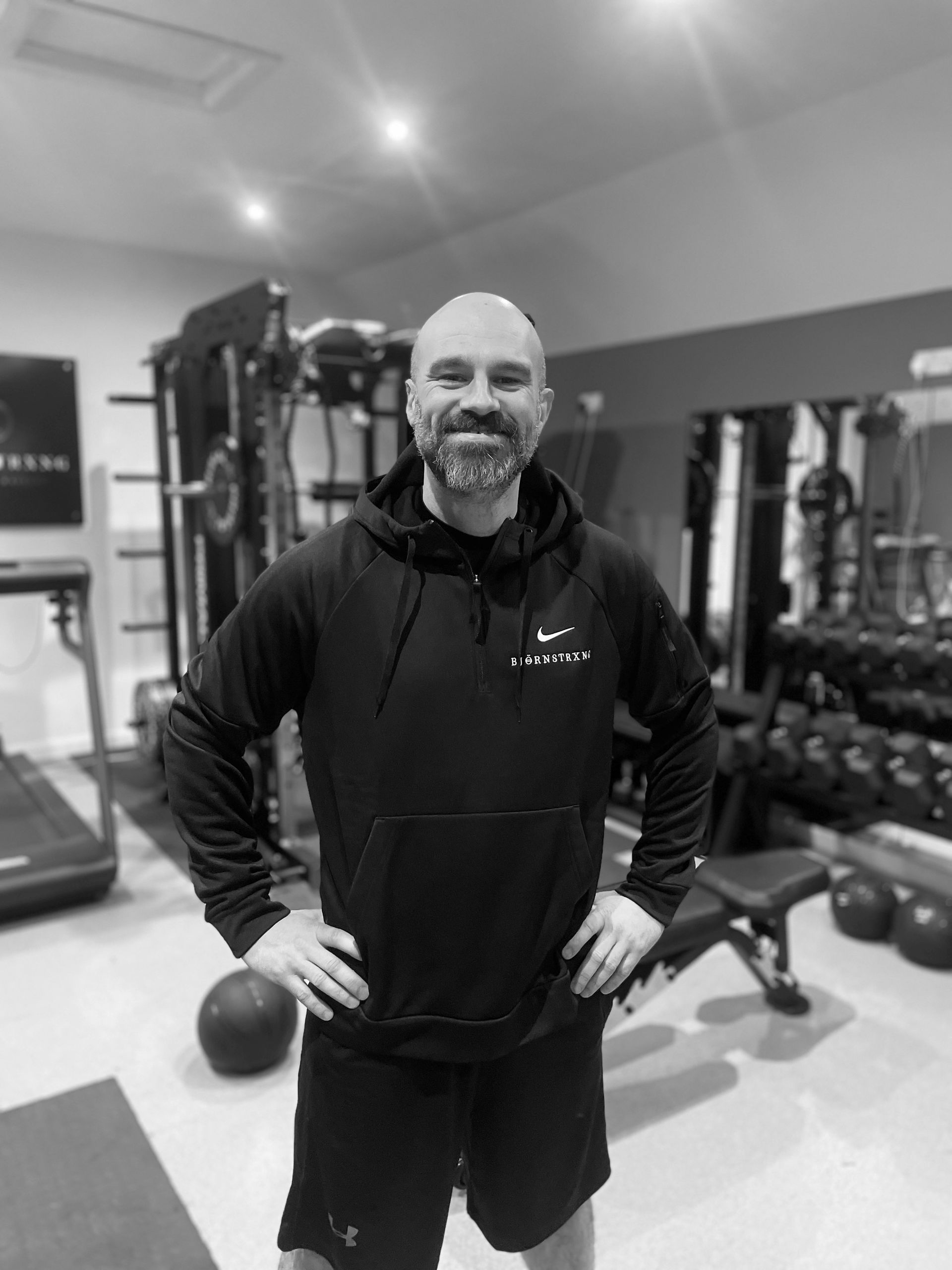 Man in black hoodie and shorts, hands on hips, in a home gym.