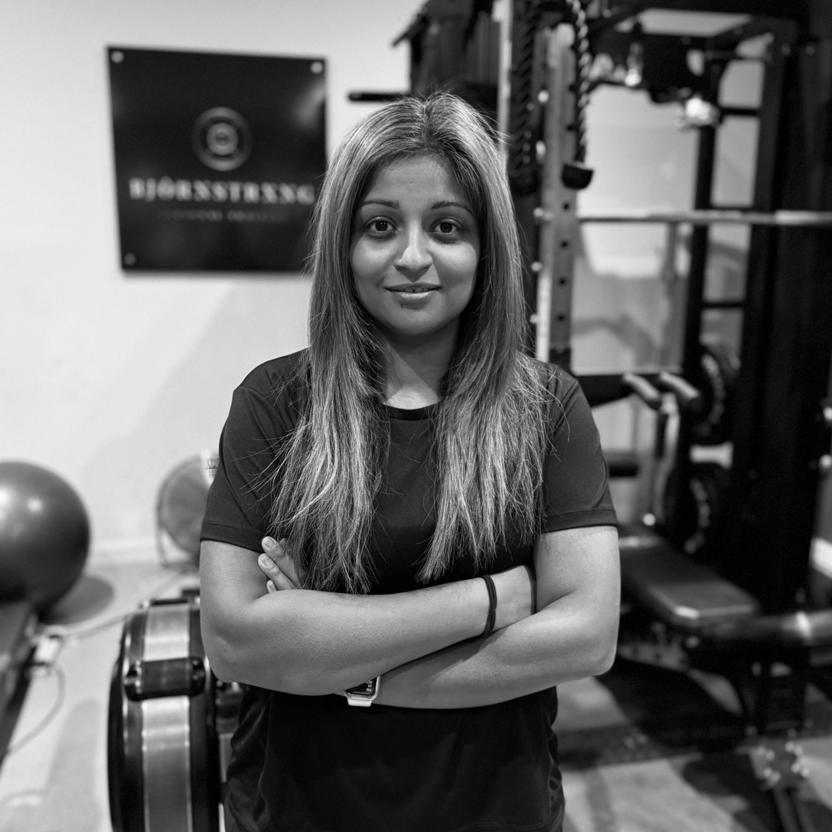 Woman with crossed arms in a gym, facing the camera. Bjornstrong logo in background.