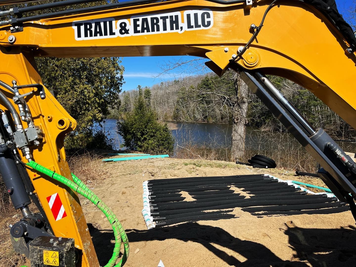 Yellow excavator with Trail & Earth, LLC logo working near a lake.