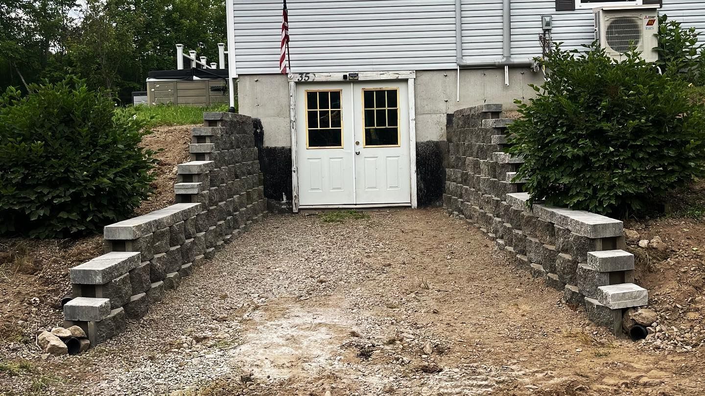 Stone retaining walls flank a gravel path leading to white double doors beneath a building.