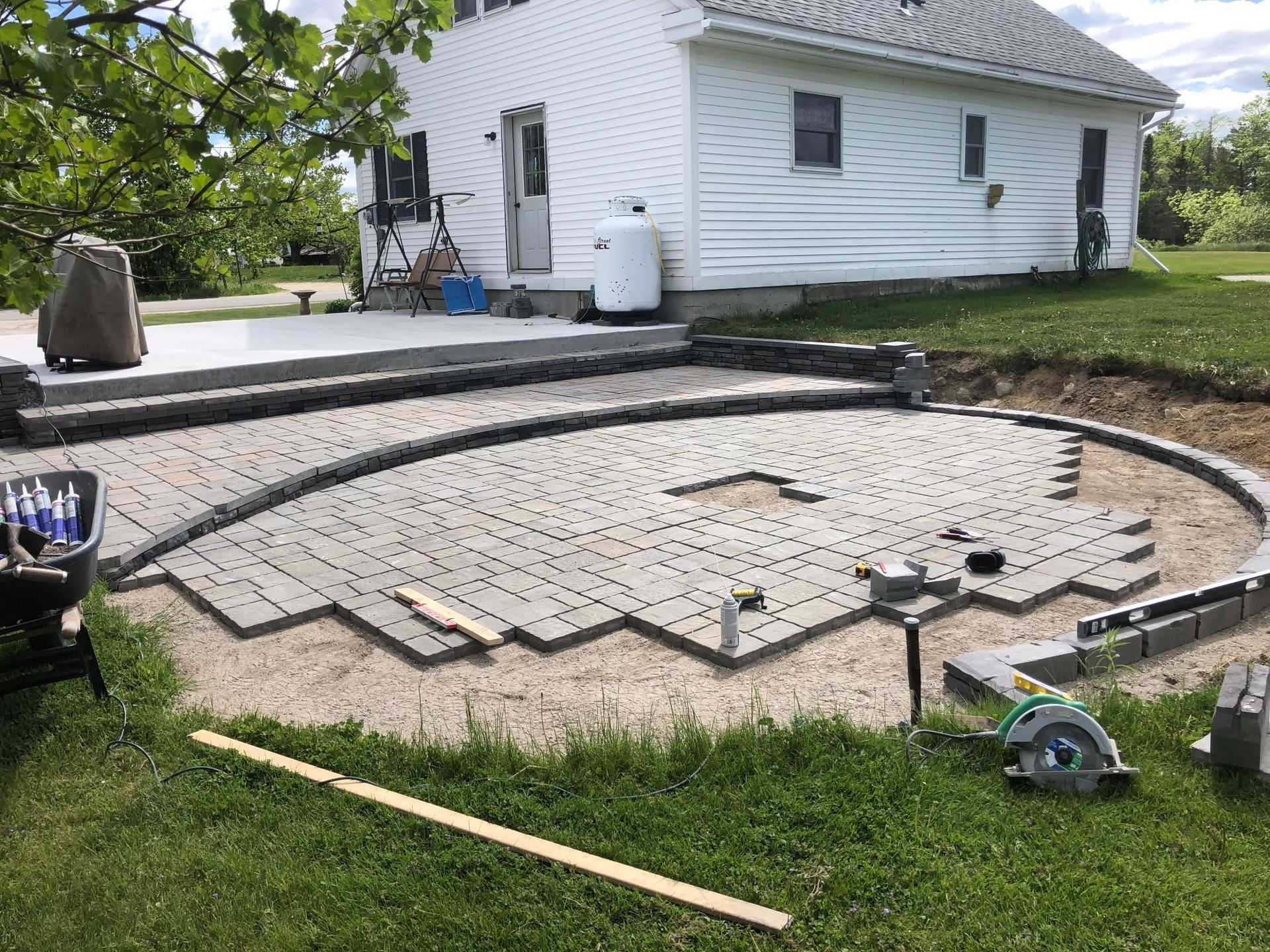 Patio under construction with gray pavers, surrounding wall, and house in background.