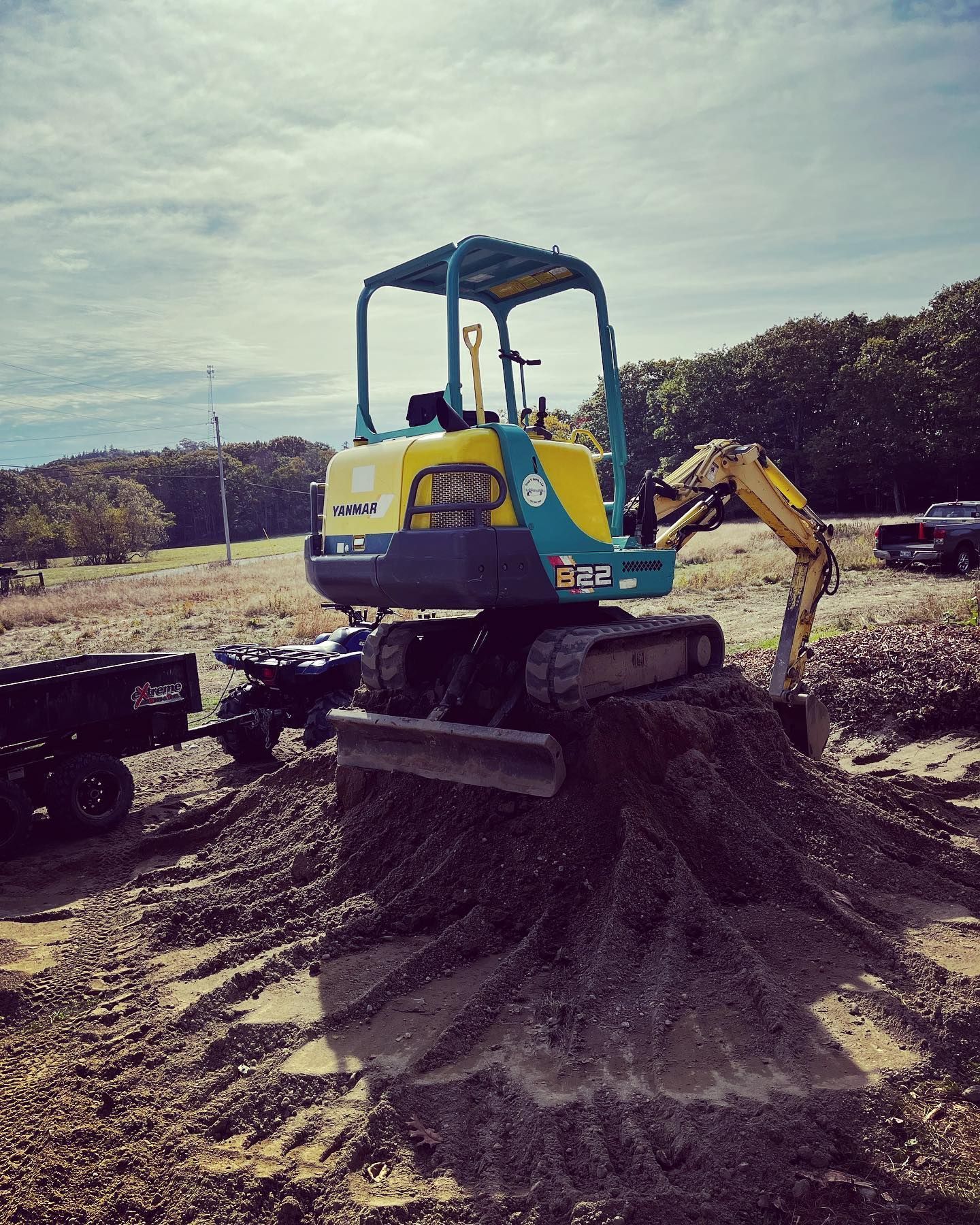 A small blue and yellow excavator on a pile of gravel outdoors.