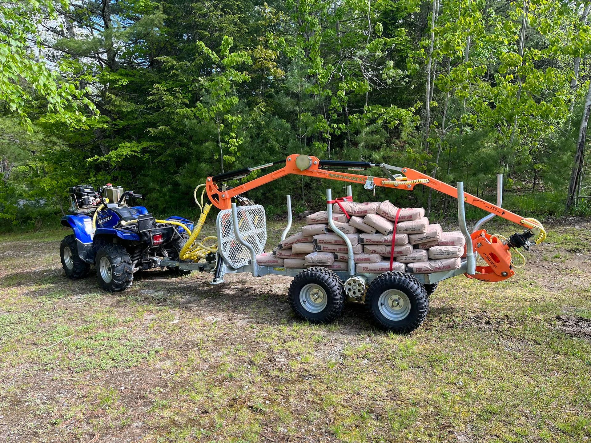 An ATV pulling a trailer loaded with bagged materials. An orange crane arm is attached to the trailer.