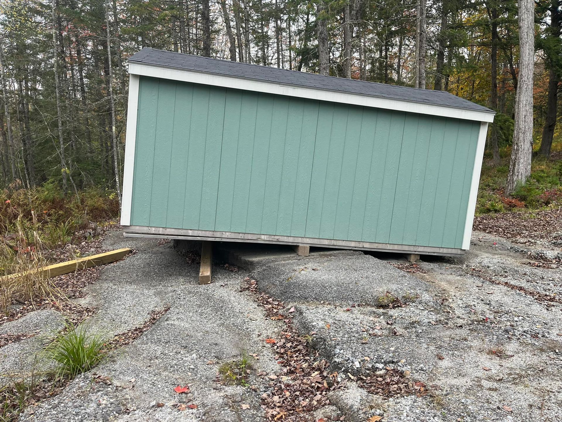Green shed on wooden beams atop a rocky surface, with trees in the background.