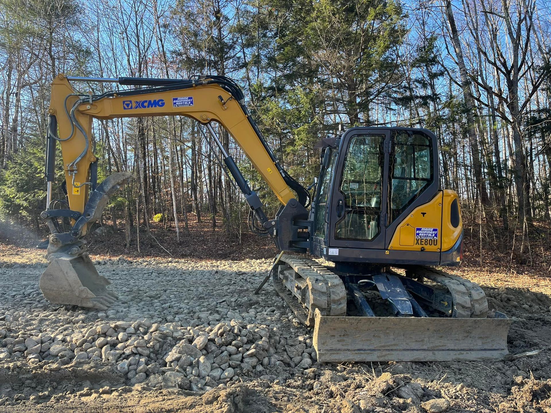 Yellow excavator on gravel in a wooded area.