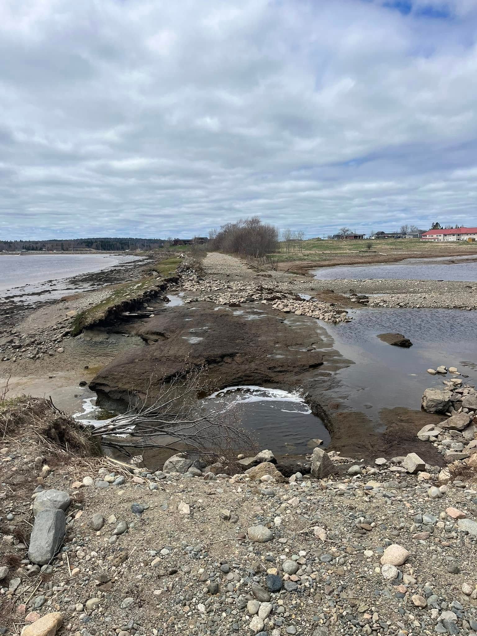 Collapsed concrete structure surrounded by water, rocks, and overcast sky.