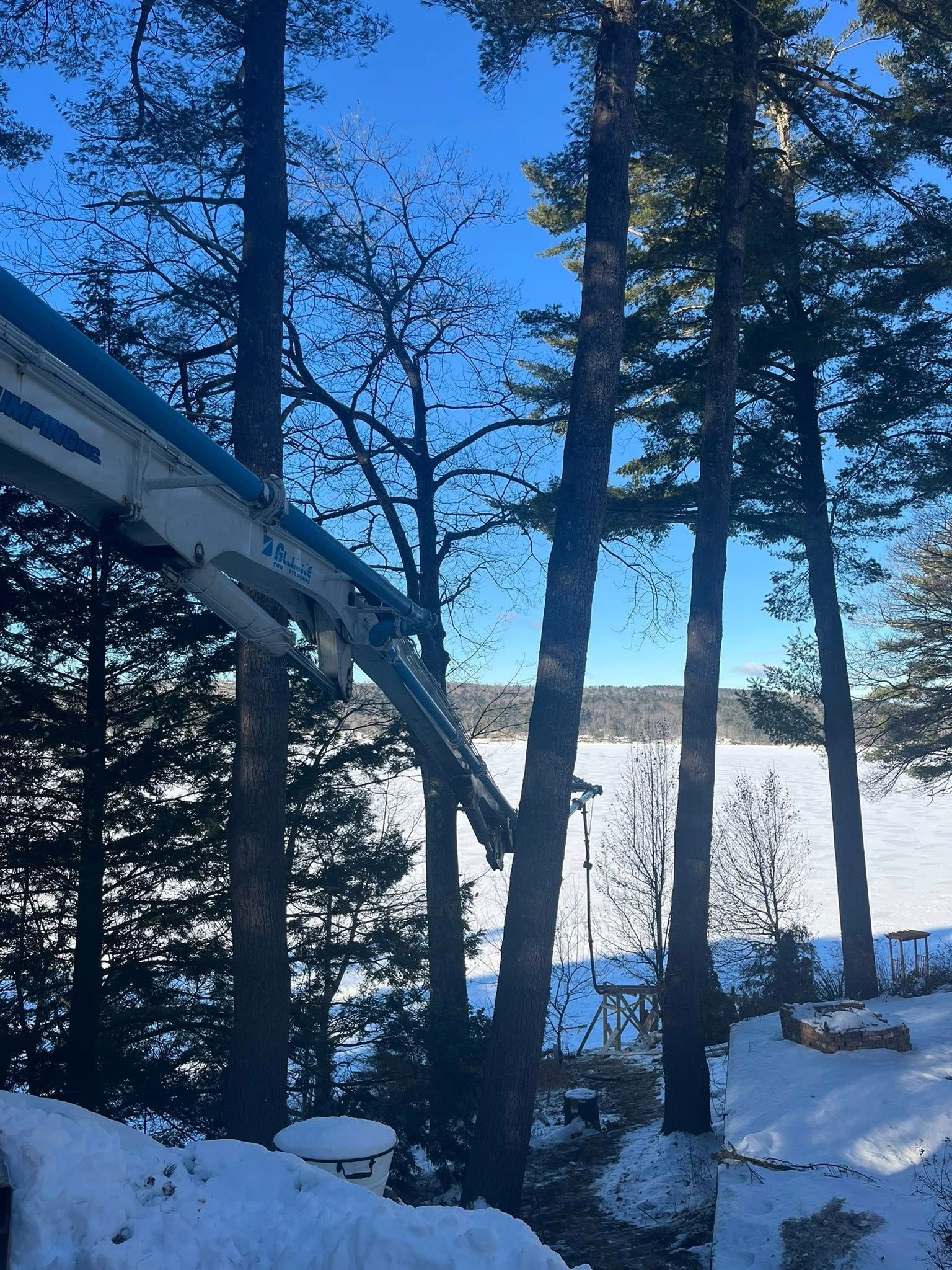 Snowy scene with trees, a lake, and a blue sky. A white crane arm extends into the frame.