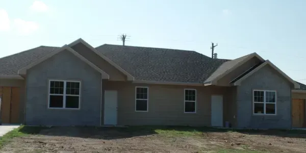 New, partially-finished duplex with gray siding, dark roof, and white doors and window frames.