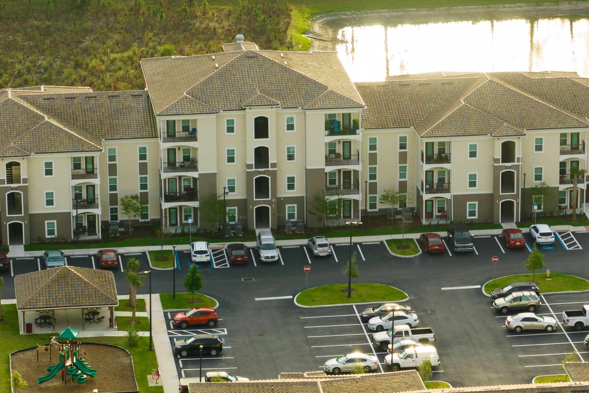 Apartment complex with parking lot, playground, and pond in background.