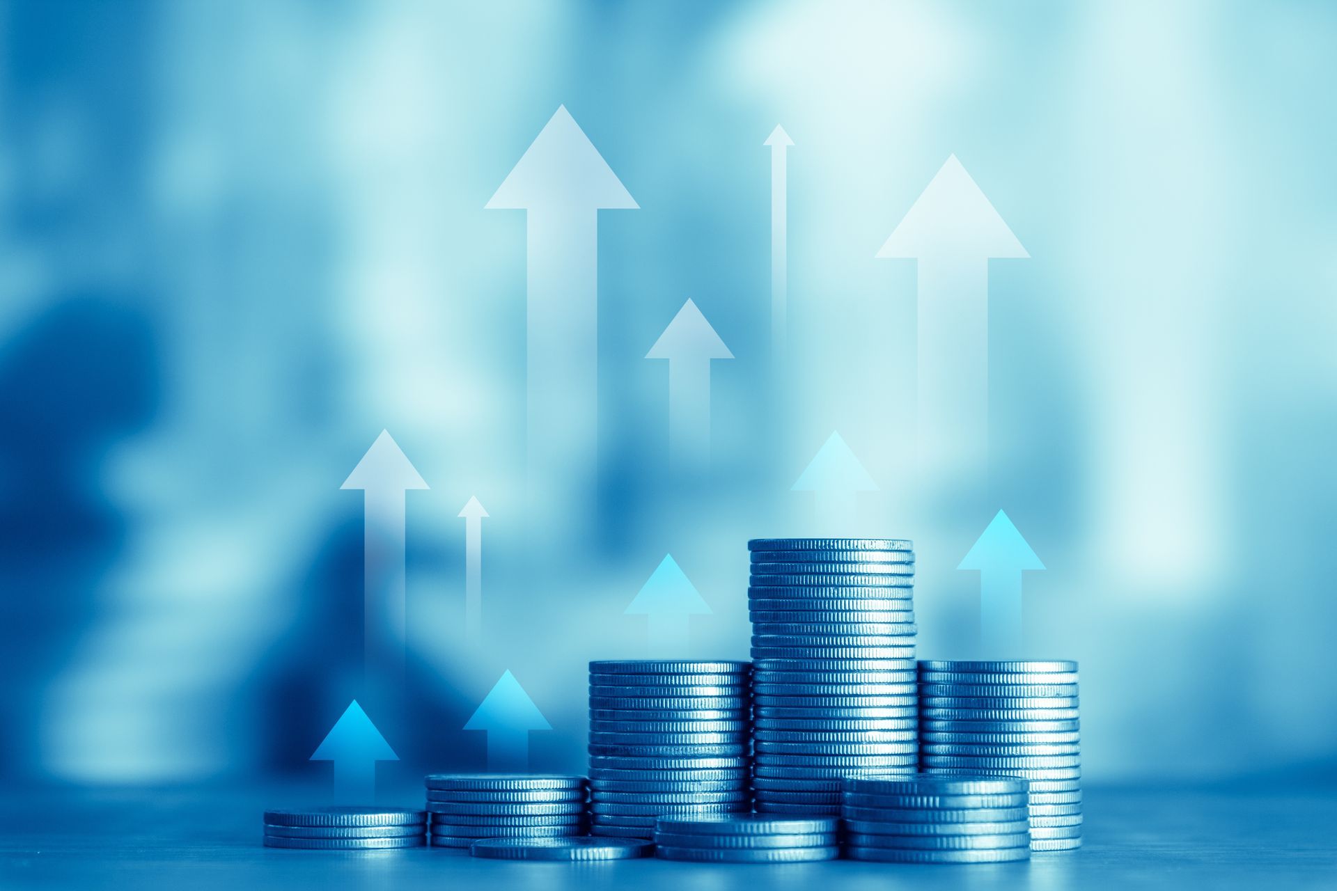 Stacks of coins with upward-pointing white arrows, set against a blurred blue background, symbolizing financial growth.