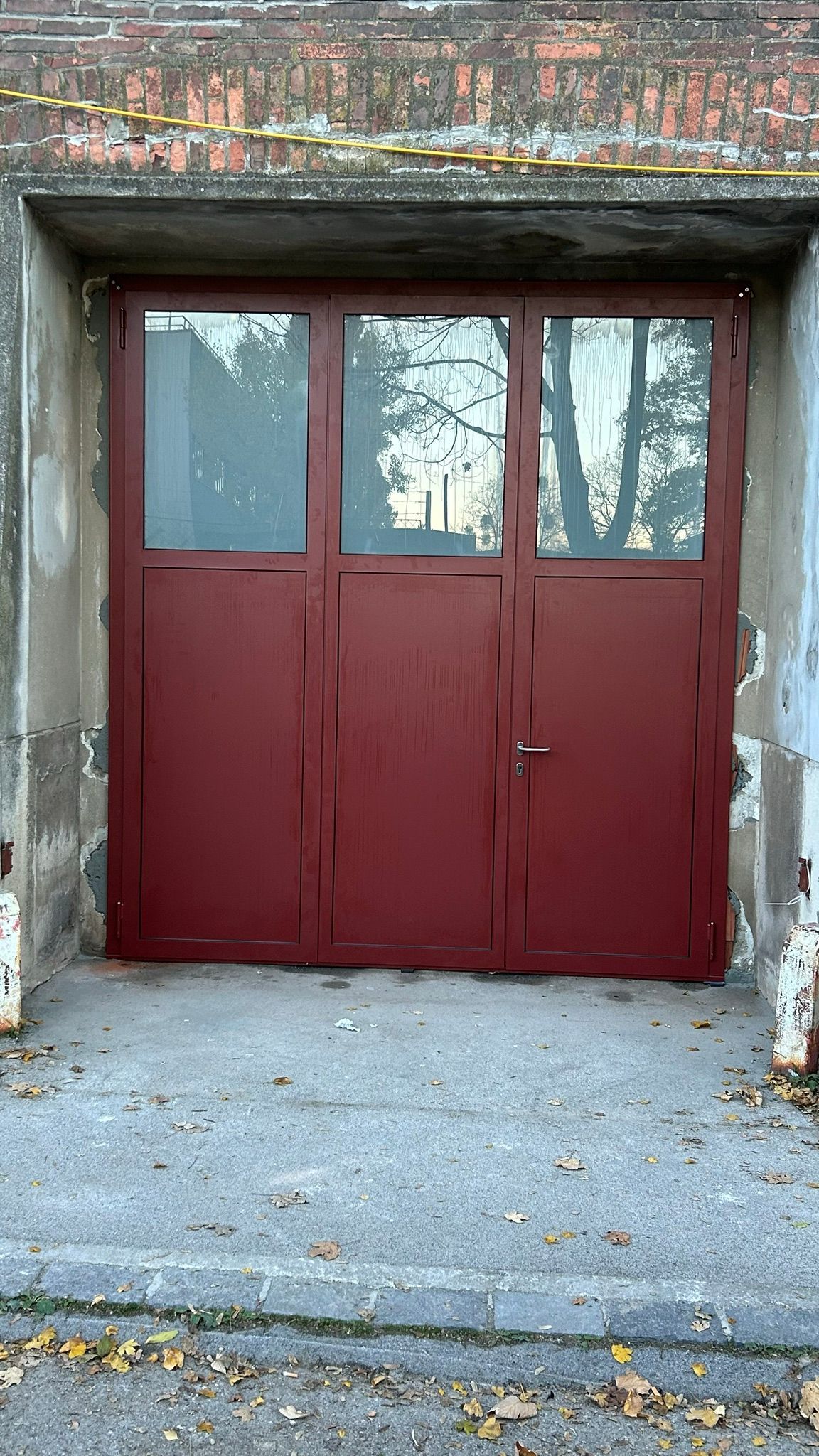 Rote Metalltür mit Glaseinsätzen in einem Türrahmen aus Ziegeln und Beton.