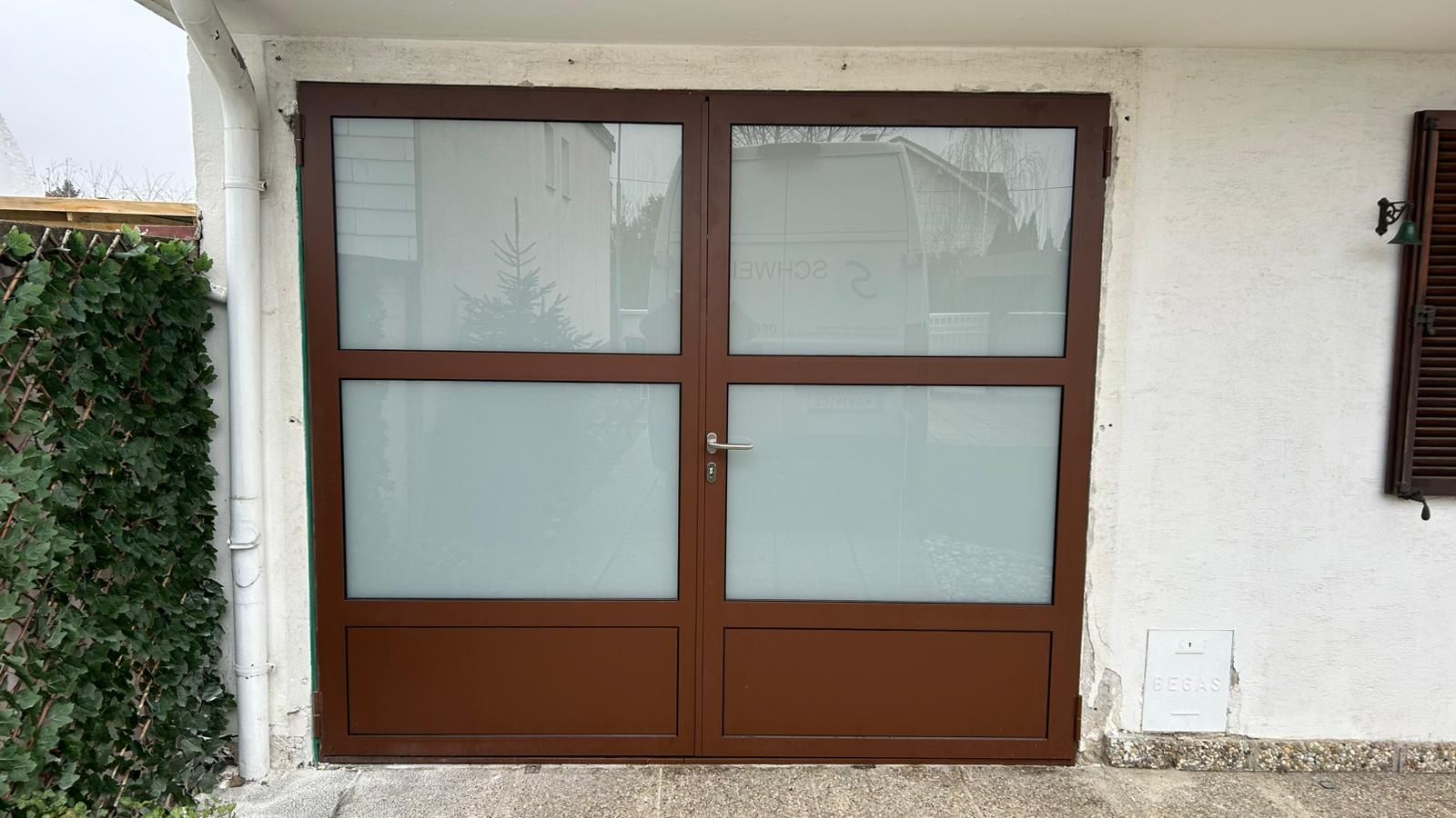 Vor einem weißen Gebäude befindet sich ein braunes Garagentor aus Metall