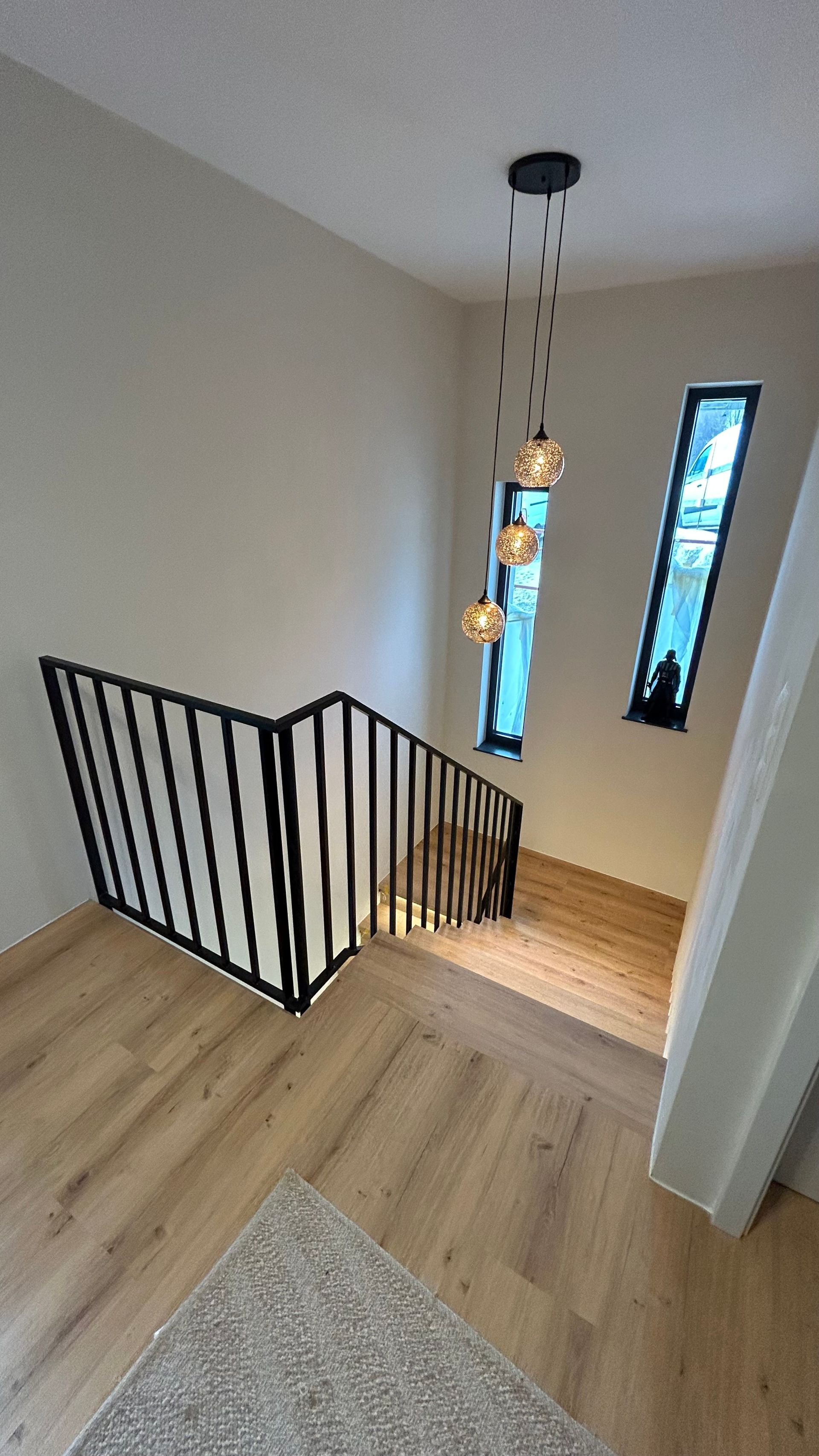 Treppe mit schwarzem Geländer, Holzboden und dekorativen Pendelleuchten in der Nähe der Fenster.