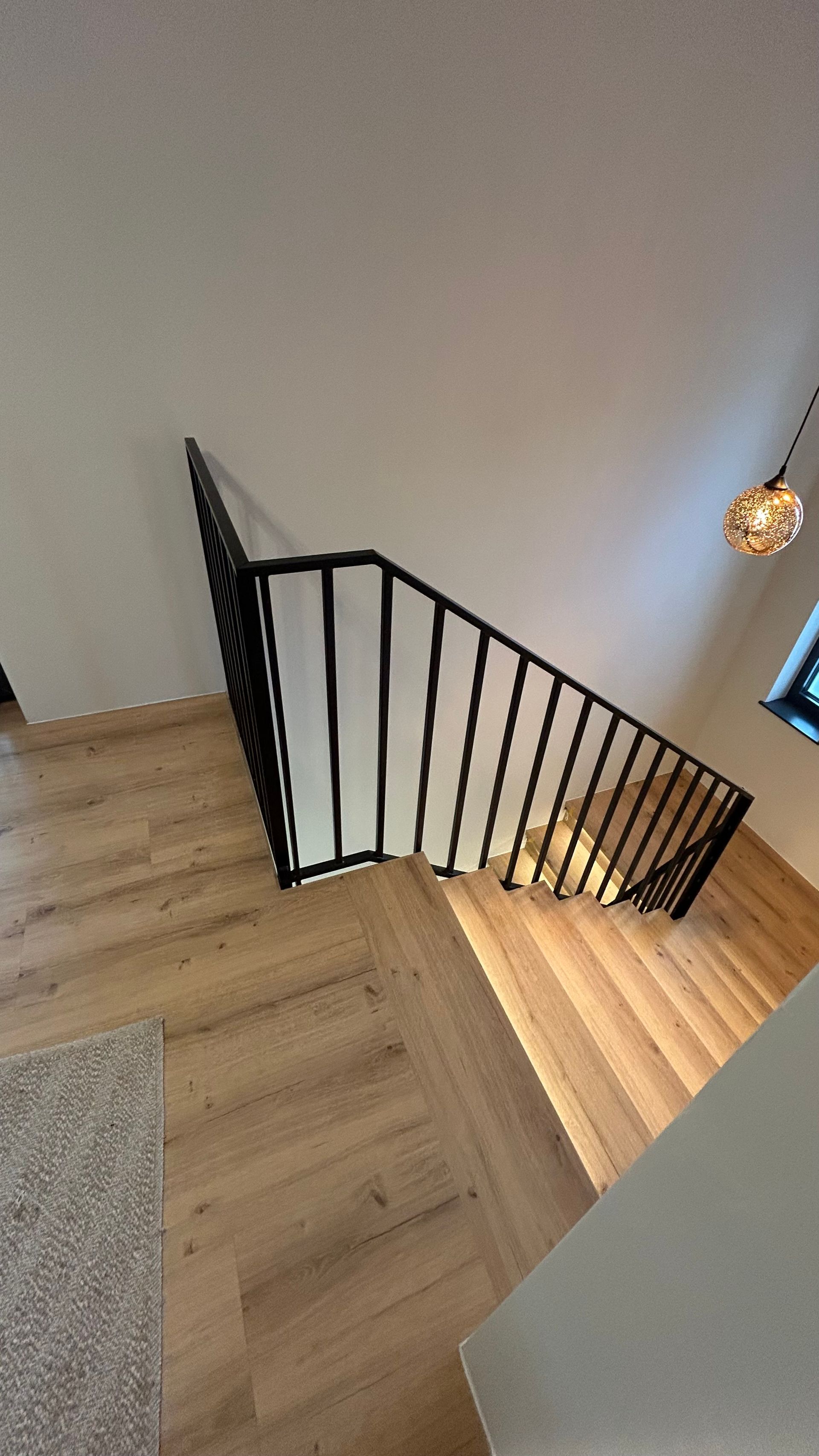 Treppe mit schwarzem Geländer und Holzstufen, die von einer oberen Ebene hinunterführt.