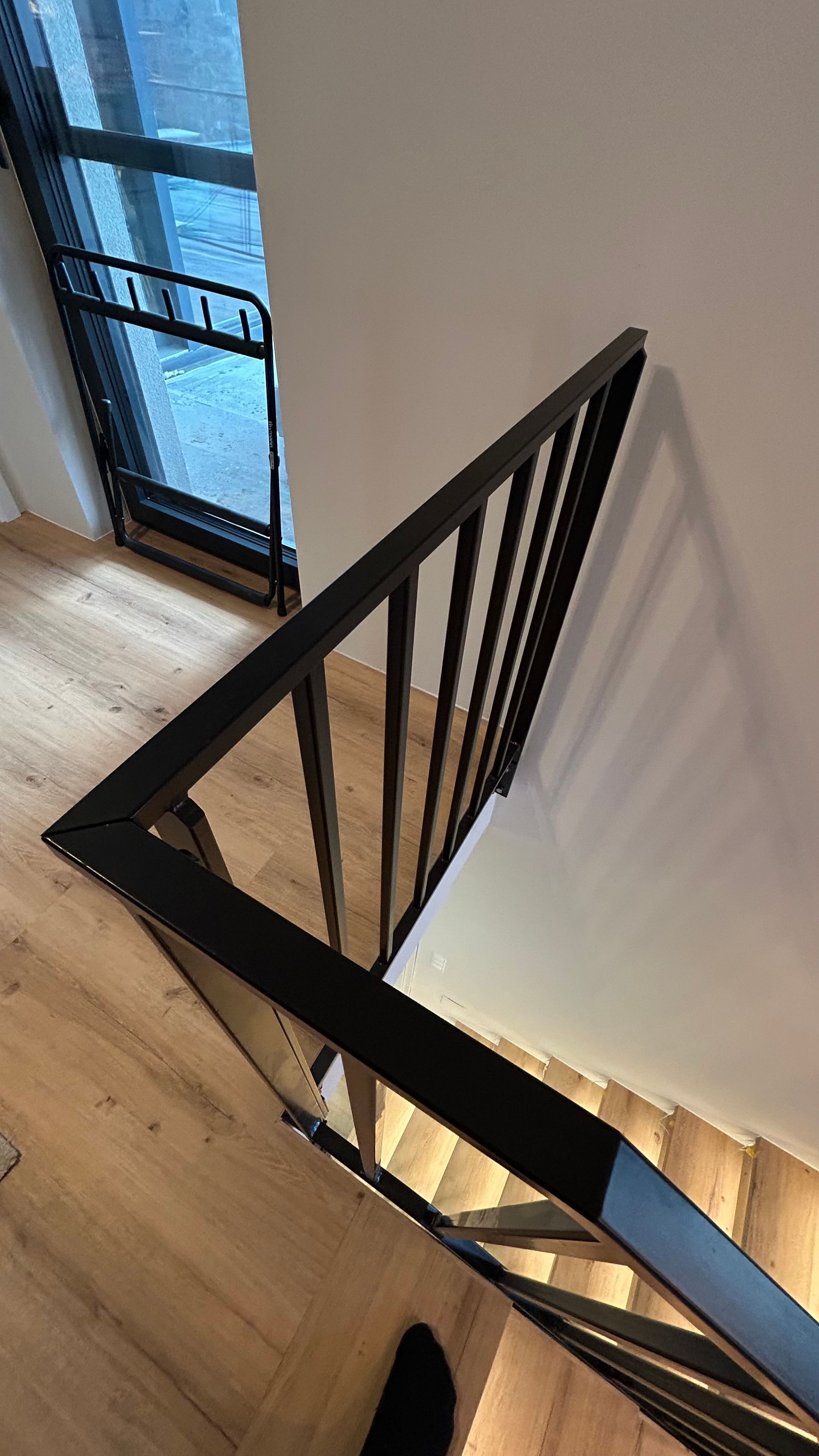 Schwarzes Metallgeländer entlang einer Holztreppe. Schräge Ansicht von oben.