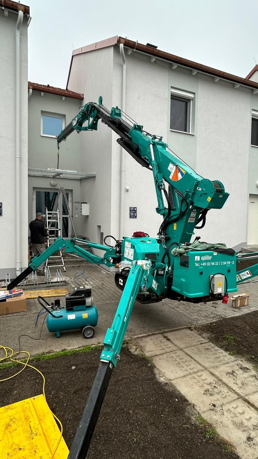 Vor einem Gebäude steht ein grüner Mini-Kran in Verwendung.