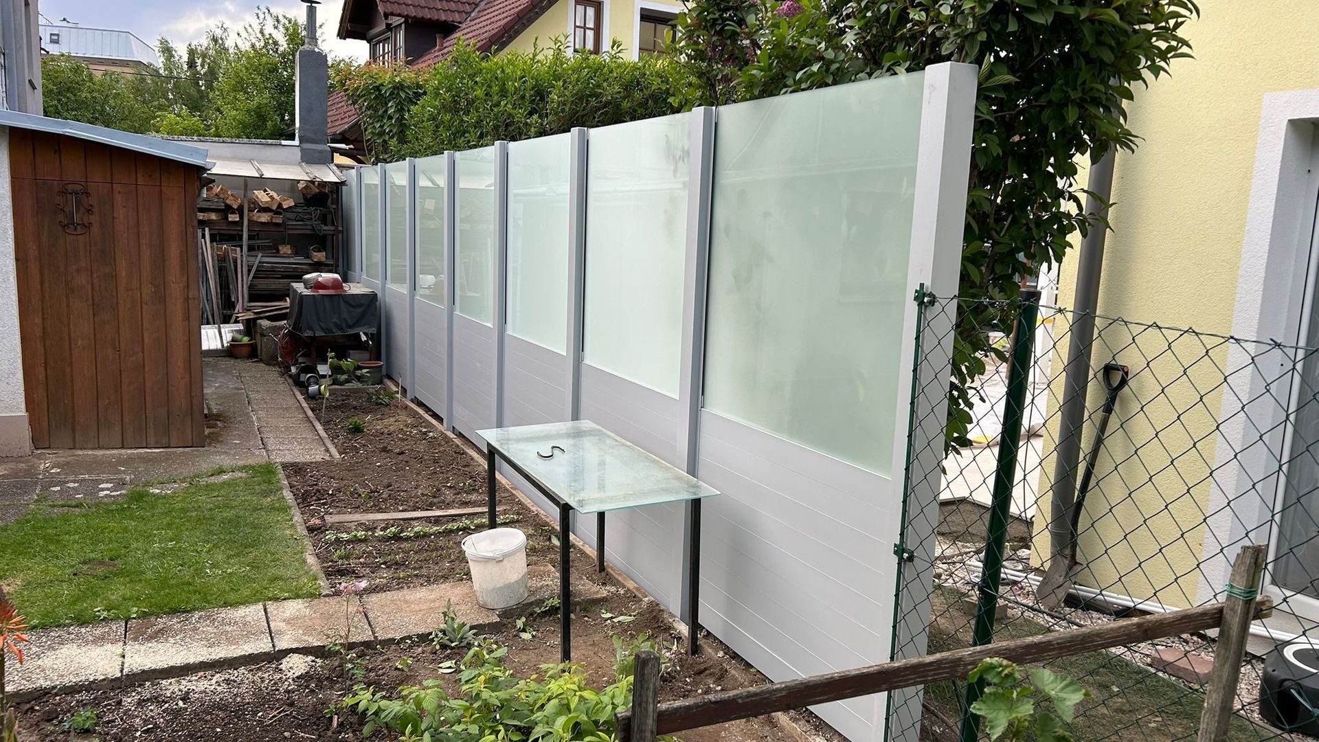 Ein Garten mit einem Sichtschutzzaun und einem Tisch vor einem Haus.