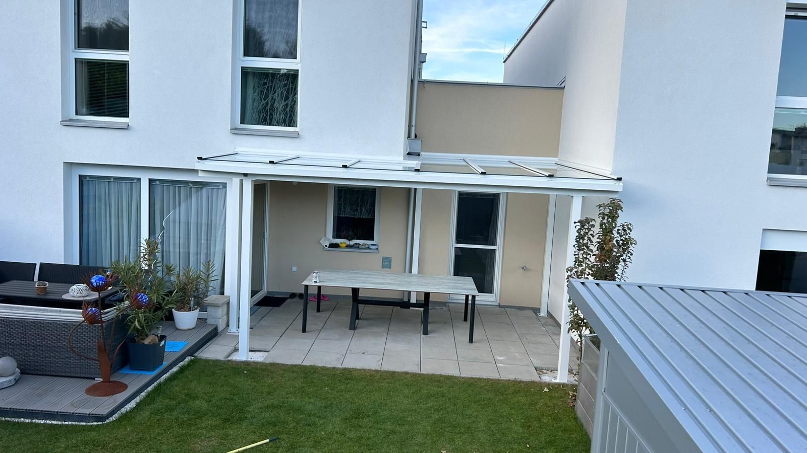 Ein weißes Haus mit einer Terrasse, einer Terassenüberdachung und einem Tisch davor